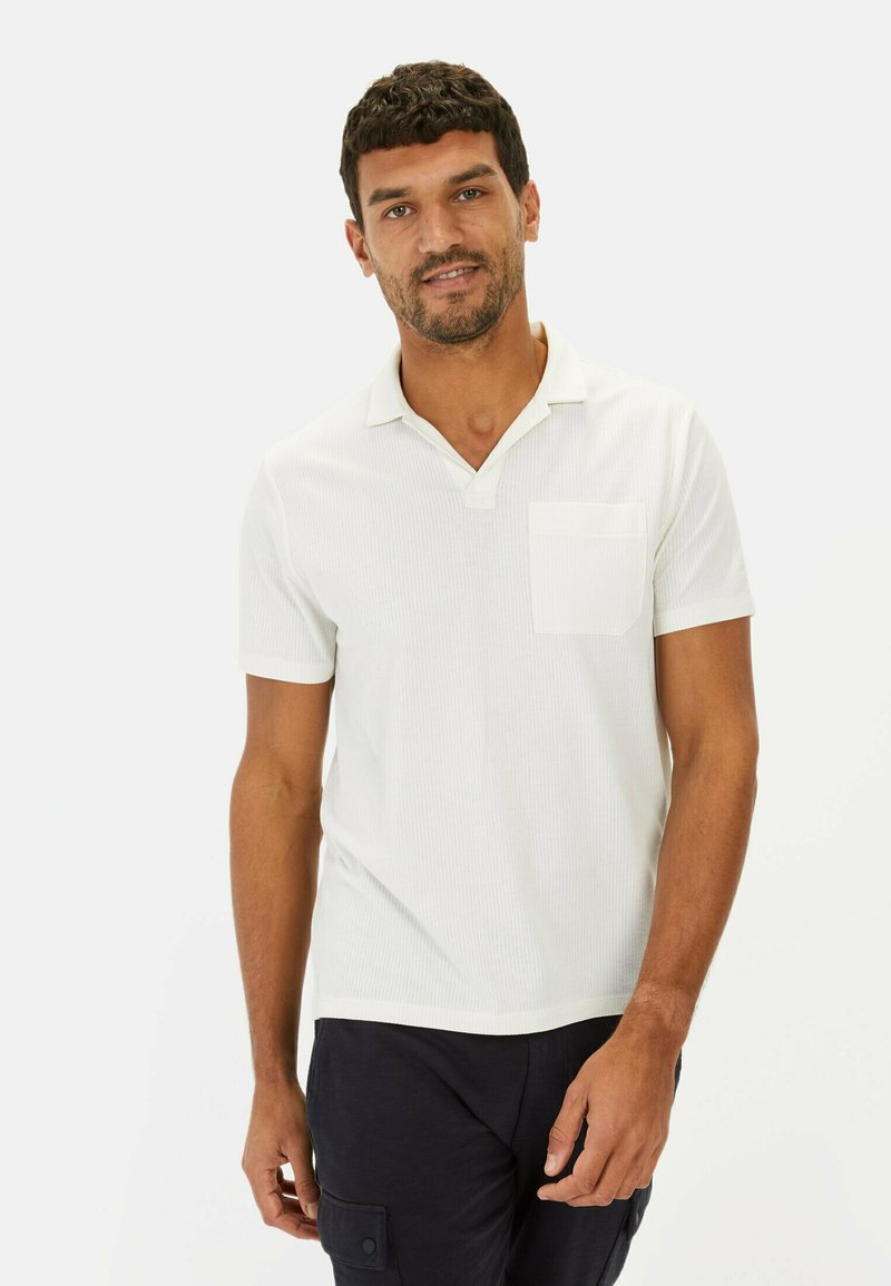 Hvid kortærmet polo shirt med et tekstureret materiale, der har en krave og en lille brystlomme. Simpelt design, afslappet pasform.