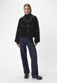 Svart texturerad jacka med krage, framknäppning med knappar och kontrasterande sömmar. Kombinerad med mörkblå vida jeans och svarta skor.