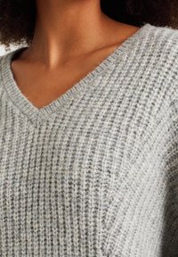 V-Ausschnitt, gestrickter Pullover in Hellgrau mit strukturierter Rippenoptik. Hergestellt aus einer Mischung weicher Fasern, die dezente Farbnuancen zeigt.