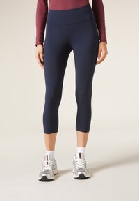 Leggings cortos de color navy hechos de una tela suave y elástica, con una cintura alta y detalles de costura sutiles, combinados con zapatillas deportivas y calcetines blancos.