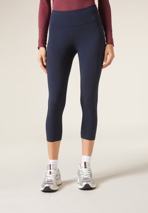 Navyfarbene, kurze Leggings aus glattem, dehnbarem Stoff mit hohem Bund und dezenten Nähtelementen, kombiniert mit Sportschuhen und weißen Socken.