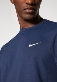 Marineblå T-skjorte med korte ermer laget av mykt stoff, med en hvit Nike-logo på brystet. Enkel rund halslinje og jevn tekstur.