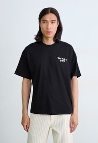 T-shirt en coton noir avec un col rond, arborant le logo blanc "Dickies 1922" sur la poitrine gauche. Conçu avec une coupe décontractée.