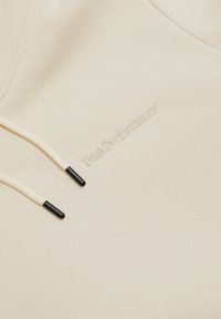Felpa beige realizzata in morbido tessuto, con cordini crema con punte nere e logo ricamato "Peak Performance".