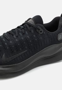 Černá běžecká obuv Nike s pleteným svrškem, černými tkaničkami a texturovanou podrážkou na bílém pozadí, šikmý boční pohled.