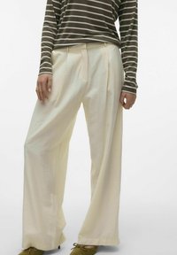 Pantalons larges crème avec des plis et des poches latérales, associés à un haut rayé marron à manches longues. Tissu lisse et léger.