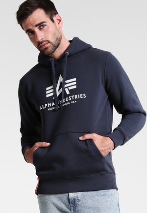 Sudadera con capucha de color azul marino hecha de una tela suave. Cuenta con un bolsillo delantero, puños elásticos y un gran logo blanco en el pecho.