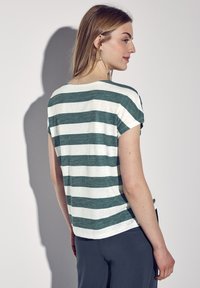 T-shirt a righe verde e bianche, maniche corte, vestibilità rilassata, realizzata in tessuto leggero. Vista di schiena, abbinata a pantaloni scuri.