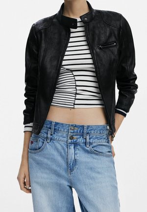 Persona que lleva una chaqueta corta de cuero negra sobre un top corto a rayas en blanco y negro, combinada con vaqueros de talle alto azul claro con doble botón.