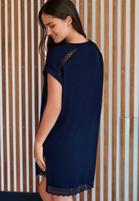 Robe courte bleu marine en tissu doux avec des accents de dentelle aux manches et à l'ourlet, présentant une coupe décontractée et des fentes latérales.