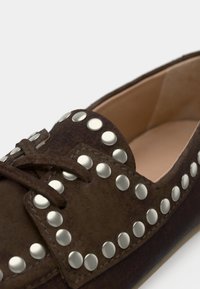 Καφέ καστόρινο παπούτσι με ασημένιες στρογγυλές τρουκς κατά μήκος των άκρων, με σχέδιο δέσιμου με κορδόνια και λεία εσωτερική επένδυση.