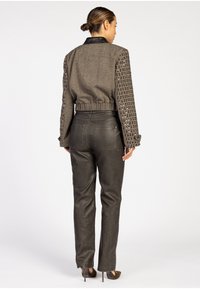 Kurz geschnittene Jacke aus strukturiertem grauem Stoff mit schwarzem Lederkragen und genagelten Ärmeln, kombiniert mit hochtaillierten schwarzen Lederhosen.