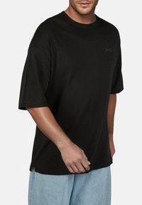Zwarte katoenen T-shirt met korte mouwen, ronde hals en een ontspannen pasvorm. Kenmerkt een subtiele logo-accent op de borst.