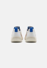 Baskets avec une tige en cuir blanc, des accents en mesh beige, des languettes de talon bleues et des semelles en caoutchouc texturé crème. Design léger et sportif.