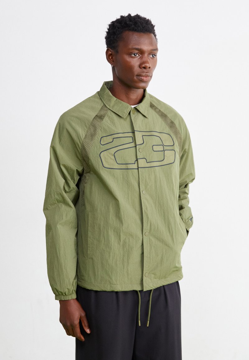 Ελαφρύ μπουφάν ελιάς με κουμπιά μπροστά, ανάγλυφες λεπτομέρειες και μεγάλη γραφική εκτύπωση. Διαθέτει ελαστικούς μανσέτες και κορδόνι στο στρίφωμα.