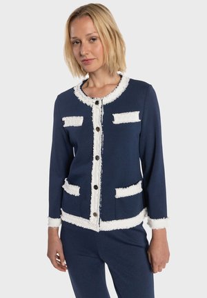 Granatowy sweter rozpinany z białą postrzępioną lamówką, okrągłym dekoltem i przednimi kieszeniami. Posiada zapięcia na guziki i wyraźną, dopasowaną konstrukcję.