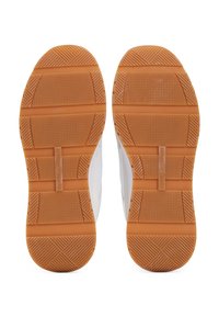 Paire de baskets blanches vues par le dessous, avec des semelles en caoutchouc marron texturées offrant une bonne adhérence, et la marque "Tommy Hilfiger".