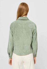 Groene corduroy jas met kraag, geribbelde textuur en knoopmanchetten. Heeft een rechte snit en een rugstukdetail.