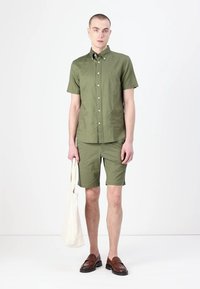 Oliwkowa, krótko-sleeve, koszula na guziki z pasującymi szortami, wykonana z lekkiego materiału. Brązowe buty wsuwane i beżowa torba na ramię.