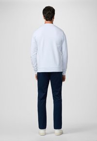 Sudadera blanca con cuello redondo, combinada con pantalones azul marino oscuros. El corte es relajado y los materiales parecen suaves y cómodos.