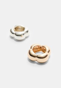 Deux anneaux : l'un en argent poli, l'autre en or rose poli. Les deux présentent une forme florale avec des bords arrondis et des centres creux.