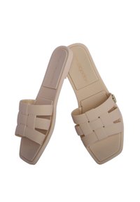 Sandalias deslizantes beige con un diseño de tira trenzada, puntera cuadrada, suela plana y un pequeño acento dorado en una de las tiras. Hechas de material suave.