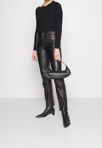 Sac en cuir noir avec une forme courbée et une courte anse. Porté avec un pull noir ajusté et un pantalon en cuir noir, stylisé avec des bottines à talons pointus.