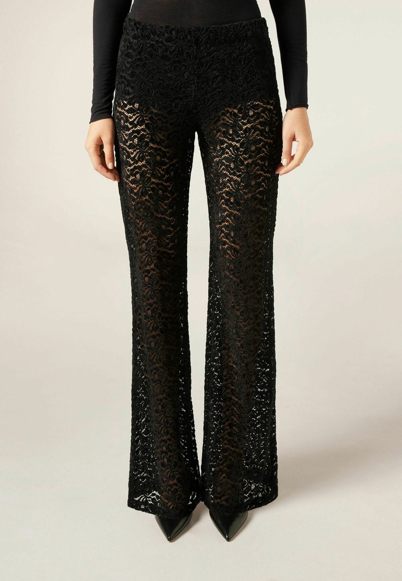 Zwart kanten broek met een bloemenpatroon, uitlopende vorm en hoge taille. Ontworpen met een doorschijnende textuur, gecombineerd met puntige zwarte hakken.