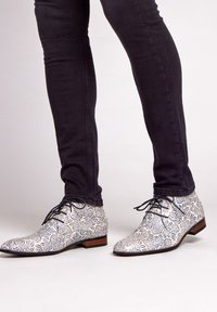 Witte dresschoenen met een blauw bloemmotief, lage hak en zwarte veters, gecombineerd met donker slim-fit jeans. Glad textuur, afgeronde neus ontwerp.
