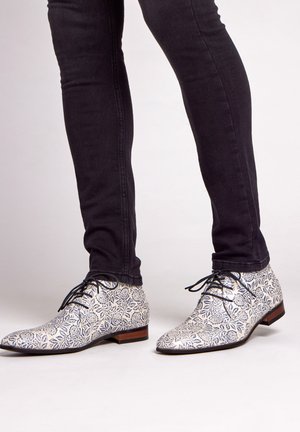 Witte dresschoenen met een blauw bloemmotief, lage hak en zwarte veters, gecombineerd met donker slim-fit jeans. Glad textuur, afgeronde neus ontwerp.