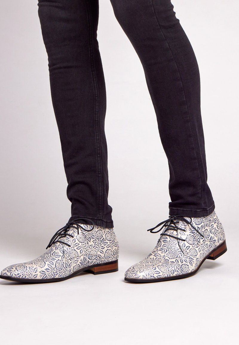 Witte dresschoenen met een blauw bloemmotief, lage hak en zwarte veters, gecombineerd met donker slim-fit jeans. Glad textuur, afgeronde neus ontwerp.