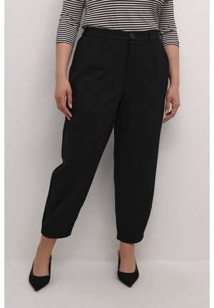 Vrouw draagt zwarte, hooggetailleerde taps toelopende broek en zwarte puntige pumps, gecombineerd met een zwart-wit gestreept topje.
