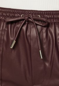 Szorty z sztucznej skóry w kolorze burgundowym, z elastycznym pasem i sznurkiem. Charakteryzują się srebrnymi elementami metalowymi oraz gładkim, teksturowanym materiałem.