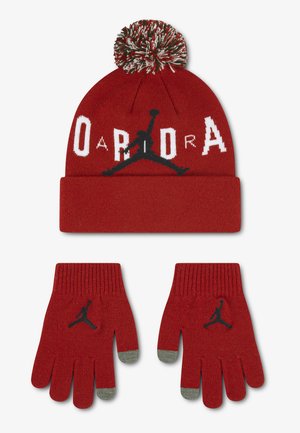 Rode gebreide muts met een pompon en bijpassende handschoenen, beide met het Jumpman-logo en de tekst "Jordan" in wit en zwart. Handschoenen hebben grijze vingertoppen.