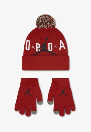 Cappello di lana rosso con pompon e guanti abbinati, entrambi con il logo Jumpman e il testo "Jordan" in bianco e nero. I guanti hanno le punte delle dita grigie.