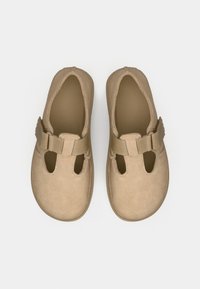 Tan suède schoenen met een ronde neus, ovale openingen en een stoffen band over de wreef. Platter zool, minimalistisch ontwerp; geen versieringen.