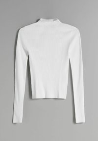 Vit ribbad långärmad tröja med hög hals liggande platt på en grå yta, som visar en slim fit och texturerade vertikala linjer.