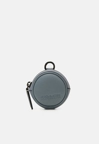 Liten rund blå läderpung med dragkedja och svart nyckelring, präglad med "Coach Leatherware"-märke på framsidan.