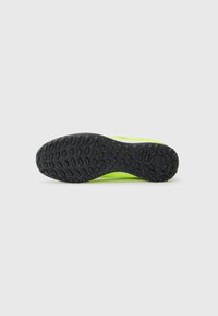 Semelle de chaussure en caoutchouc noir, texturée avec des motifs circulaires. Tige en vert fluo, présentant un design aérodynamique et des détails minimalistes.