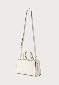 Sac à main blanc avec bordure noire, double poignées et bandoulière réglable. Comprend des détails en métal doré et de petites clous décoratifs.