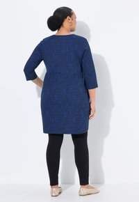 Tunic blu con motivo, maniche tre quarti, vita peplum, abbinata a leggings neri e scarpe beige a slip-on. Tessuto morbido e vestibilità rilassata.