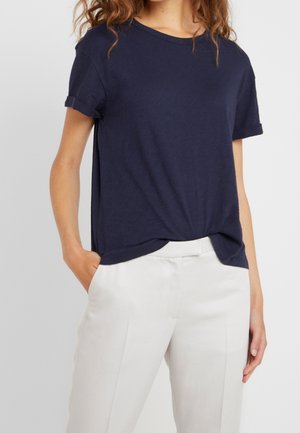 Marinblå t-shirt med kort ärm i lätt material, rund halsringning, avslappnad passform med upprullade ärmar, tillsammans med ljuskrämfärgade skräddarsydda byxor.