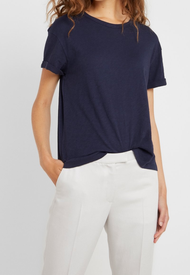 Marineblå kortærmet t-shirt i let stof, rund halsudskæring, afslappet pasform med oprullede ærmer, parret med lyse cremefarvede skræddersyede bukser.