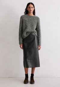 Jasnoszary włóczkowy sweter, wysoki okrągły dekolt, w zestawieniu z czarną skórzaną spódnicą midi o gładkiej teksturze oraz ciemnobrązowymi butami z skarpetkami do kostek.