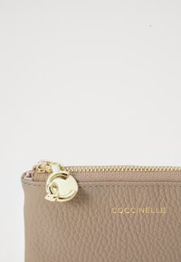 Beige leather pouch with gold hardware, zip closure, and embossed logo. Features textured surface and subtle sheen. Compact and minimalist design.