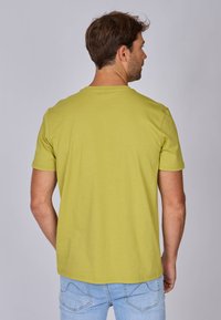 T-shirt vert clair à manches courtes avec un col rond, texture lisse et détails de couture subtils, présenté de dos.