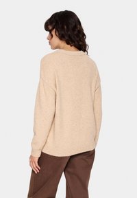 Bež kudumisega sviiter, millel on mugav lõige, soonikkoes kaelus ja tekstuuriga täpid. Kombineeritud pruunide pükstega, näidates igapäevast stiili.