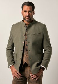Chaqueta de lana verde con cuello alzado, cierre de botones y bolsillos laterales inclinados. Presenta una sutil textura y detalles de botones marrones.