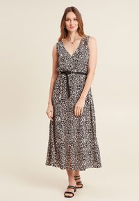 Maxikleid mit Leopardenmuster, V-Ausschnitt, ärmellosem Design, Taillengürtel und gestuftem Rock, aus leichtem, fließendem Stoff. Schwarze Sandalen.
