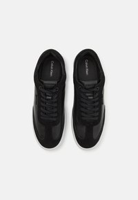 Sneaker neri realizzati con una combinazione di pelle liscia e morbida suede, dotati di un design con lacci e suole in gomma bianca.